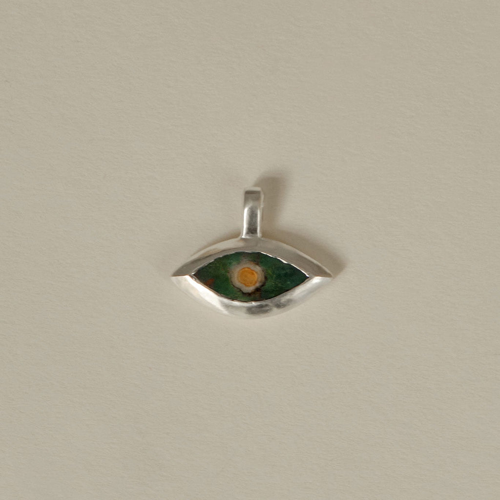 Silver eye-shaped pendant with green and orange color on a beige background