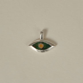 Silver eye-shaped pendant with green and orange color on a beige background