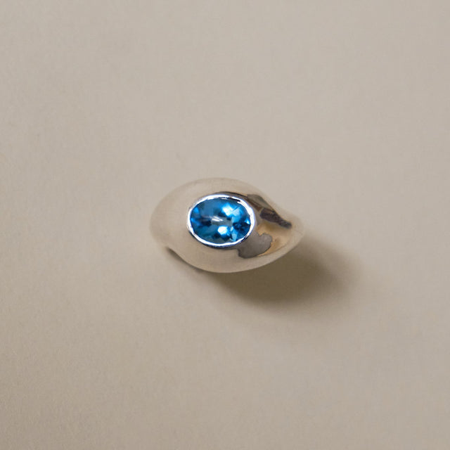 Silver ring with a blue gemstone on a beige background